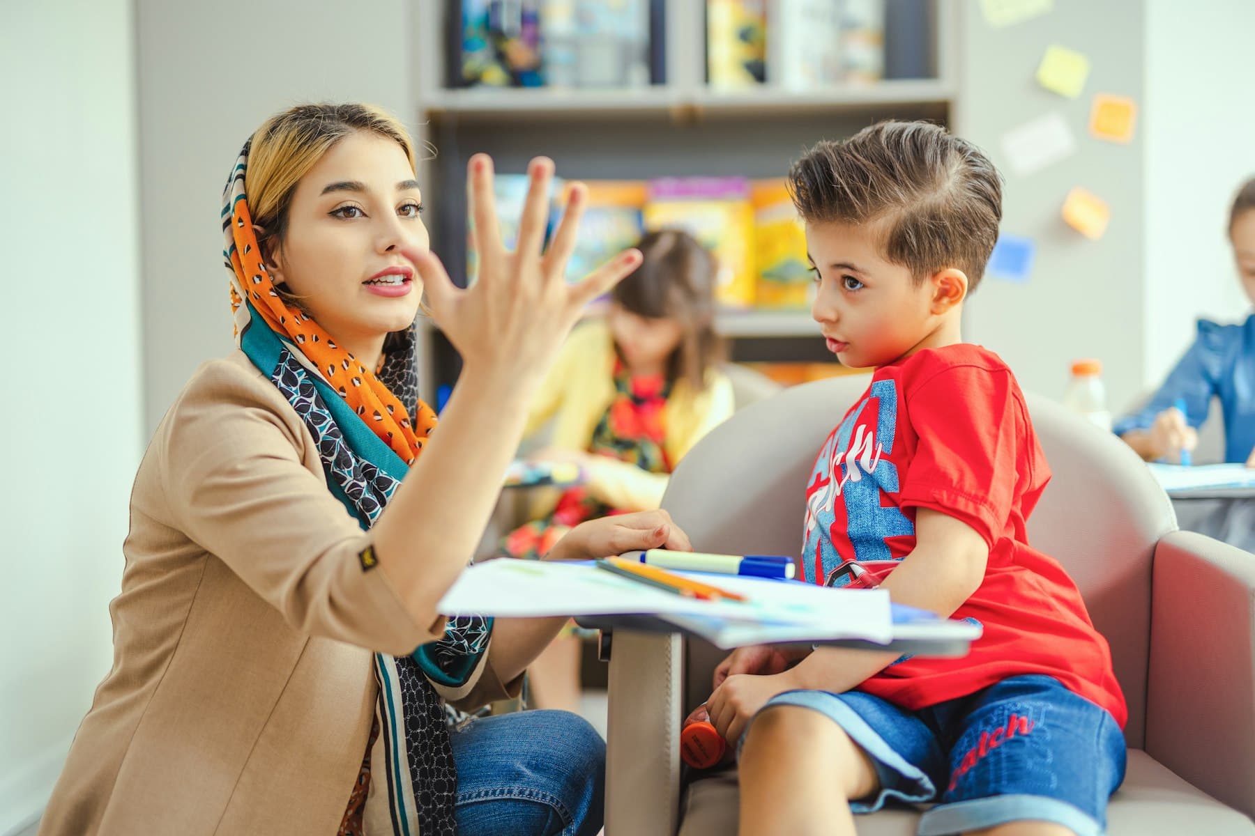A speech therapist working with a young child at a table.