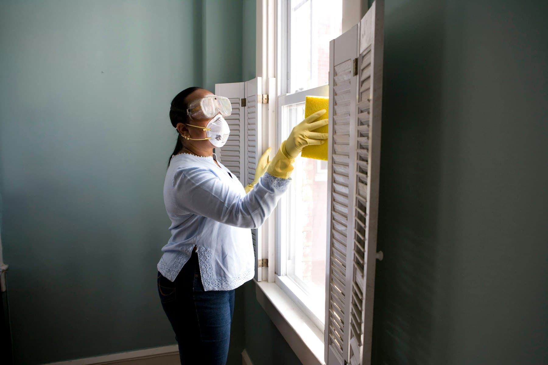 A pest control technician in a mask treating a window frame.